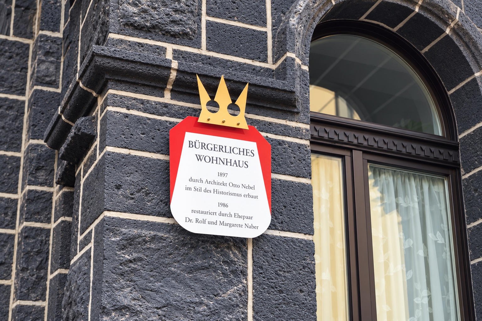 Originales rot-weißes Historienschild mit goldener Krone an einer Natursteinfassade